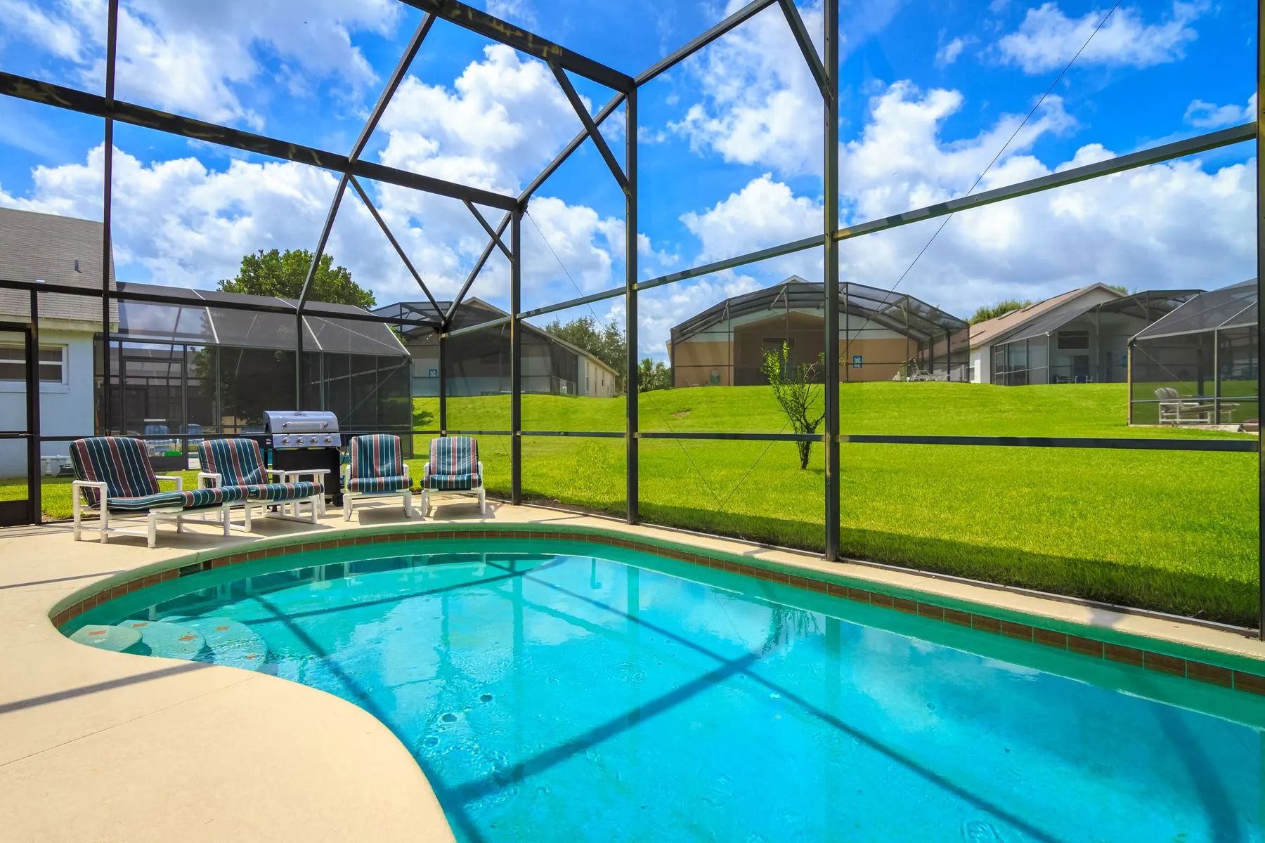 Screened pool enclosure over a pool and deck with lounge chairs behind a Florida home