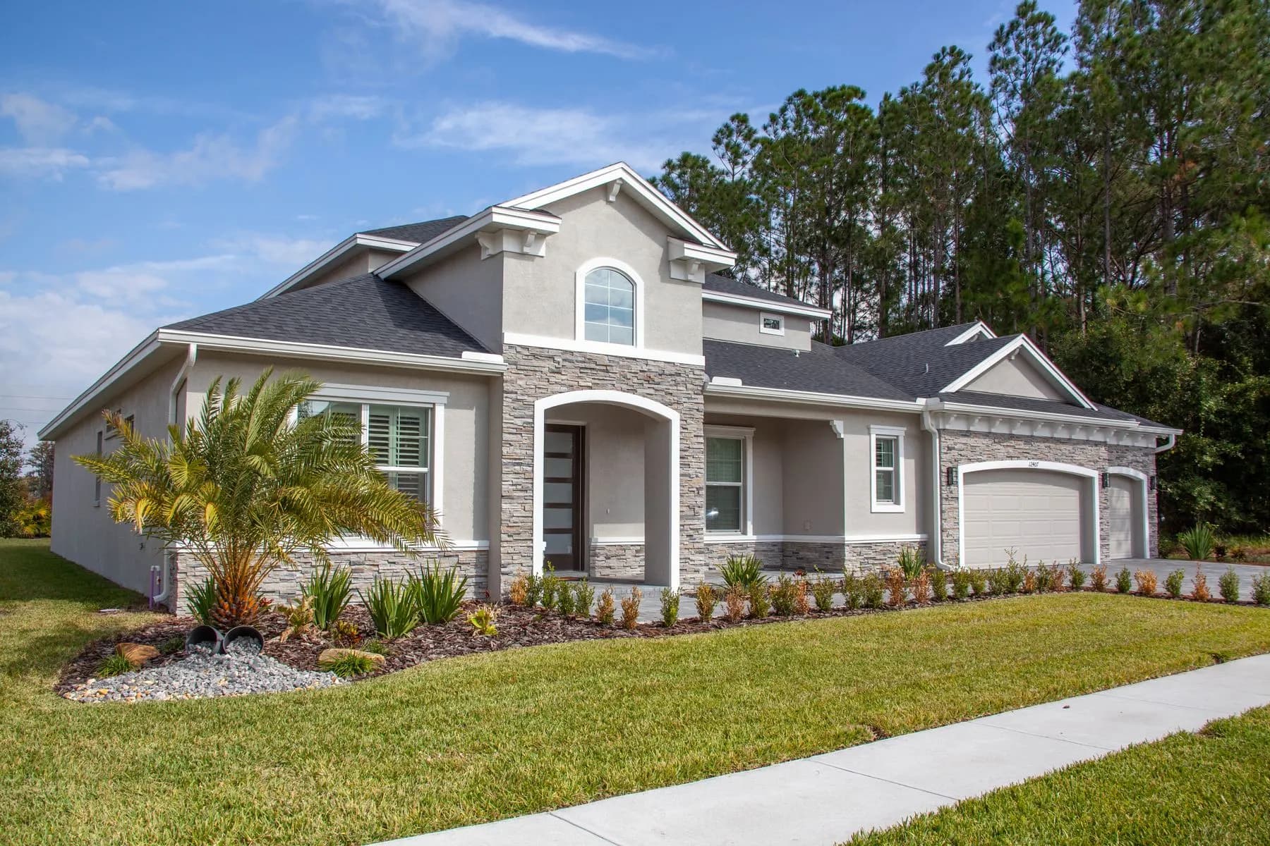 Stucco home in Florida with a stone front, arched entry, a palm and a concrete sidewalk