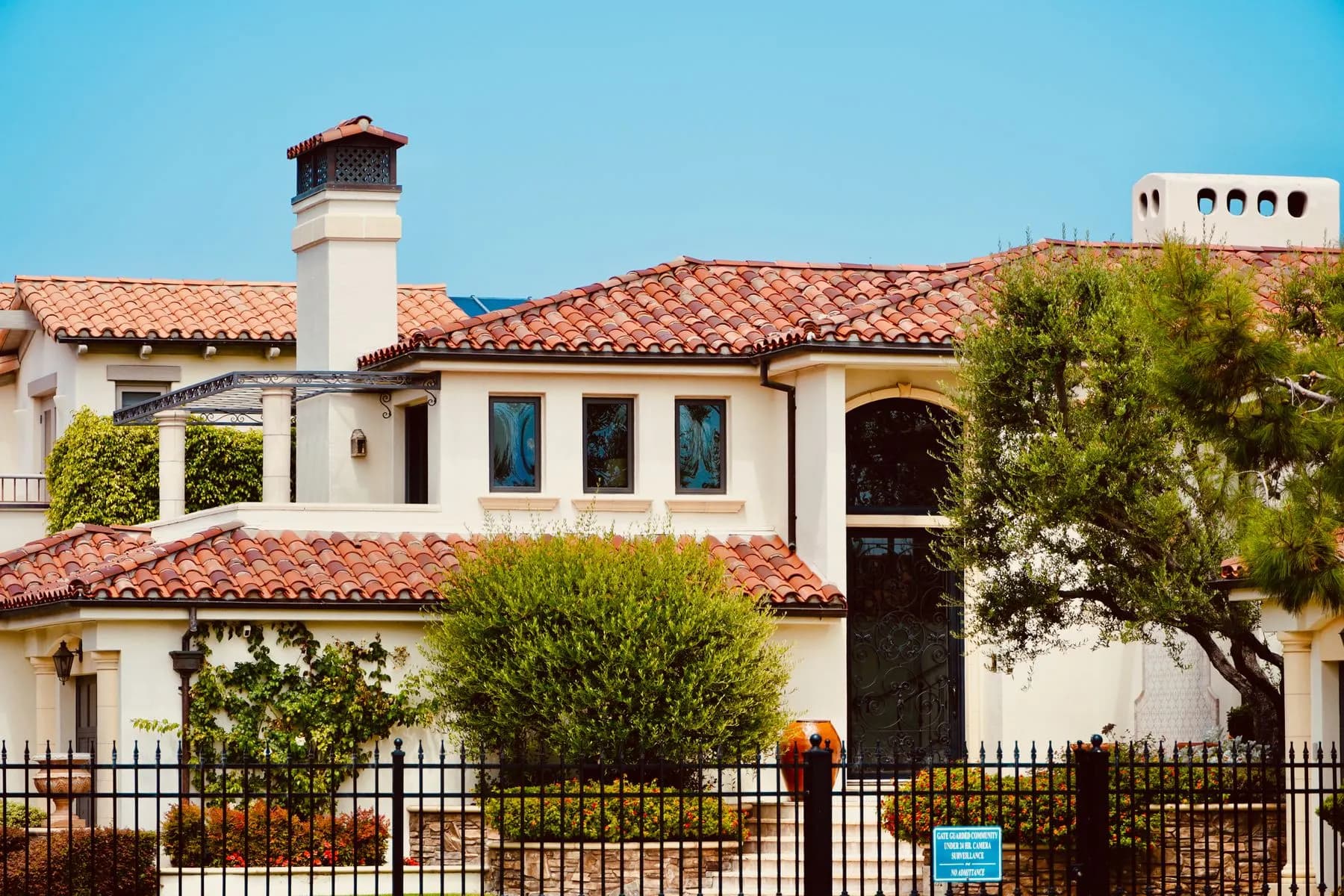 Two story Mediterranean style home with a clay tile roof behind an iron fence